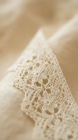 Delicate cream lace trim with intricate floral patterns on soft fabric background, close-up macro photography showcasing fine textile craftsmanship and detail.