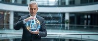 Middle-aged Caucasian businessman in suit holding glowing digital shield icon representing cybersecurity and data protection in modern office environment.