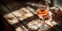 Glass of amber whiskey on rustic wooden table with warm sunlight creating dramatic shadows for luxury beverage advertising and bar concepts.