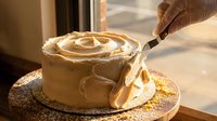 Pastry chef decorating round cake with caramel swirl using brush, professional bakery technique for dessert presentation and confectionery design.
