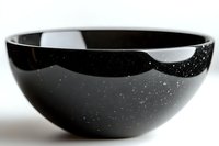 Elegant black ceramic bowl with subtle white speckles against dark glaze, photographed in minimalist style on white background. Modern tableware for contemporary dining.