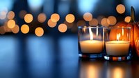Glowing candles in glass holders create cozy atmosphere against blurred bokeh lights background, romantic evening mood for spa, meditation or holiday decor.