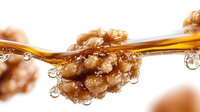 Golden honey dripping from wooden dipper with walnuts, natural sweetener flowing in droplets, organic food ingredient for healthy cooking and baking.