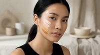 Young Asian woman applying facial cream in modern bathroom during skincare routine for beauty and wellness.