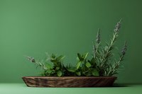 Fresh herbs including rosemary, basil and lavender arranged in rustic wooden bowl on green background for culinary and aromatherapy applications.