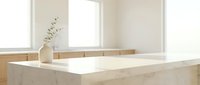 Marble countertop with dried eucalyptus in ceramic vase, bright natural light from windows, minimalist kitchen or bathroom design backdrop for product display.