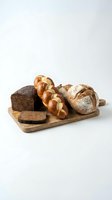 Assorted fresh baked breads including rye loaf, braided roll and artisan round loaf arranged on wooden cutting board against white background.