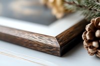 Rustic wooden frame corner with pine cone and evergreen branch detail against soft white background creates cozy winter holiday atmosphere.