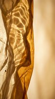 Golden sunlight streams through translucent amber fabric, casting intricate shadow patterns and creating warm, ethereal lighting effects for design and background use.