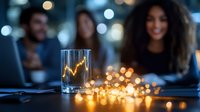 Young woman with curly hair smiling at business meeting with colleagues, focus on glass with financial chart and decorative lights on table.
