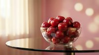 Fresh red cranberries in glass bowl on table with warm bokeh lights creating cozy holiday atmosphere for seasonal cooking and festive decorations.