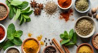 Colorful spices and herbs arranged in bowls with fresh mint leaves, cinnamon sticks, star anise on textured background for culinary cooking and seasoning.