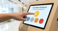 Hand touching tablet screen with customer feedback survey showing colorful emoji rating system from happy to sad faces in modern office environment.