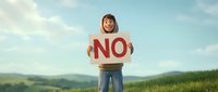 Young woman with brown hair and fair complexion holding a cardboard sign with red "NO" text in an open field landscape, expressing refusal or protest for advertising and marketing campaigns.