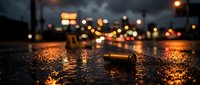 Wet asphalt street at night with glowing bokeh lights from traffic and streetlamps creating atmospheric urban scene with reflections on rainy pavement surface.
