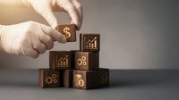 Hands in gloves arranging wooden blocks with financial icons including dollar signs and growth charts for business strategy and investment planning.