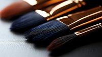 Professional makeup brushes arranged in row on dark surface with soft focus and dramatic lighting, highlighting natural bristles and wooden handles.