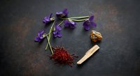 Natural herbal medicine ingredients with purple flowers, saffron threads and wooden spoon arranged on dark slate background for wellness and aromatherapy.