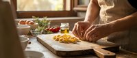 Fresh homemade pasta being prepared on wooden cutting board in warm kitchen setting with natural lighting and cooking ingredients nearby.