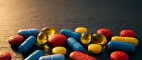 Colorful pharmaceutical pills and capsules scattered on dark surface with warm lighting for medical and healthcare concepts.