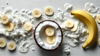 Fresh coconut and sliced banana arrangement on white background with creamy coconut flesh scattered artistically, creating tropical food composition.