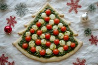 Christmas tree shaped pizza with pesto, cherry tomatoes and mozzarella balls on festive background with ornaments and snowflakes for holiday celebration.