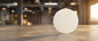 White round blank badge or sticker mockup on wooden table in modern office space with warm lighting for branding and promotional design projects.
