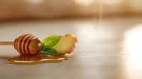 Wooden honey dipper with dripping golden honey and fresh mint leaves on light wooden surface with soft bokeh background and copy space.