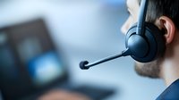 Young male customer service representative wearing wireless headset in office environment, side view close-up shot showing professional communication setup.