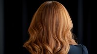 Blonde wavy hair from behind on dark background, showing professional salon hairstyle with soft curls and honey-colored highlights. Natural looking modern cut.
