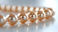 Elegant strand of lustrous peach-colored pearls in macro view showing smooth spherical surfaces with soft reflections and shadows on light background.