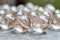 Crystal clear glass marbles with delicate internal patterns arranged on textured gray surface, creating elegant minimalist composition with soft bokeh effect.
