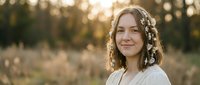 Young woman with flower crown smiling in golden hour sunlight outdoors. Natural portrait photography for lifestyle and wellness content.