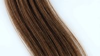 Smooth brown hair strands with natural highlights flowing diagonally across white background, showcasing healthy hair texture for beauty and salon concepts.