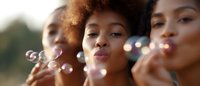 Young African American women blowing soap bubbles outdoors in warm sunlight, expressing joy and playful moments during summer leisure activity.