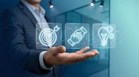 Businessman in dark suit holding hand up with glowing digital icons representing target, rocket, and lightbulb for innovation, strategy, and business growth concepts.