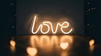 Glowing neon love sign with warm light reflection on dark background, romantic atmosphere for Valentine's Day and wedding decor.