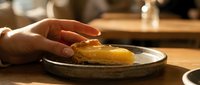 Close-up of hands placing golden pastry on rustic ceramic plate in warm kitchen setting with soft natural lighting for culinary and food presentation.