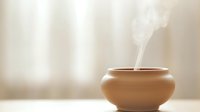 Minimalist clay aromatherapy diffuser emitting gentle steam on neutral background. Wellness and spa concept with traditional ceramic vessel for essential oils.