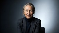 Professional mature woman with gray hair in black business suit against gradient background for corporate headshot and executive portrait photography.