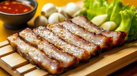 Grilled pork belly slices served on wooden cutting board with fresh lettuce, mushrooms and spicy dipping sauce, close up view of Asian cuisine preparation.