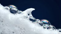 Soap bubbles floating over white foam against dark blue background creating dreamy ethereal atmosphere for spa wellness and relaxation concepts.