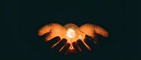 Hands holding glowing orb of light against dark background, symbolizing innovation, energy, power, and shared vision for business and technology concepts.
