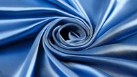 Luxurious blue silk fabric swirled in elegant spiral pattern with soft folds and glossy sheen texture creating dynamic movement and flow for fashion design background.