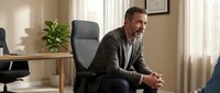 Confident middle-aged Caucasian businessman in suit sitting in modern office interior with natural lighting and professional atmosphere.