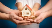 Family hands protecting wooden house model symbolizing home insurance, real estate investment and property protection concept on blue background.