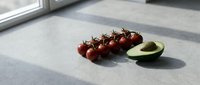 Fresh cherry tomatoes on vine and halved avocado on gray stone countertop in natural sunlight, healthy eating concept.