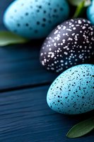Speckled Easter eggs in turquoise blue and dark purple colors arranged on navy wooden background with green leaves, creating festive spring holiday mood.