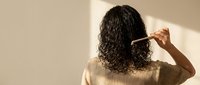 Woman with curly hair combing locks in sunlit room, self-care routine and hair maintenance concept for wellness and beauty lifestyle content.