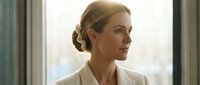 Professional blonde businesswoman in white blazer looking confidently out office window during golden hour lighting for corporate presentations.